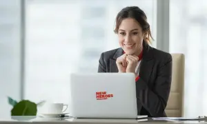 Uśmiechnięta kobieta w garniturze patrzy na laptopa z logo "New Heroes Academy".